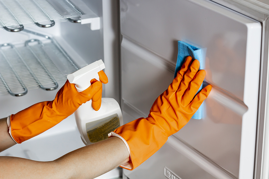 female hands in protective gloves are wiping refrigerator inside using a spray